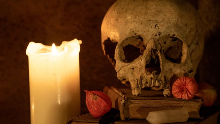 A close-up of a skull next to a burning candle in a spooky, dimly lit room.