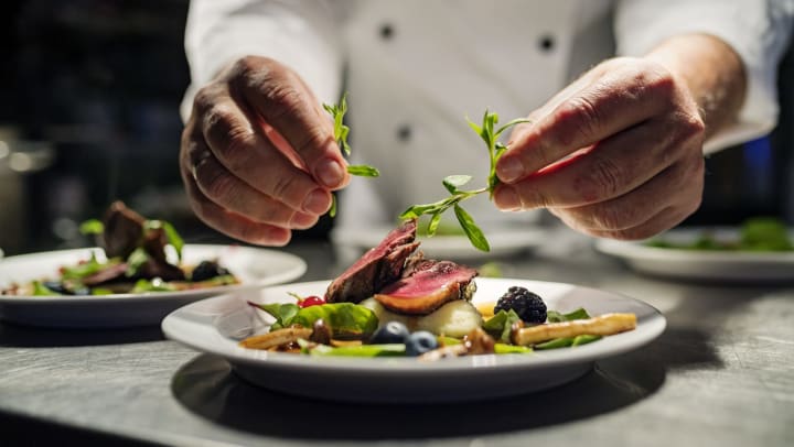 Close-up of a chef garnishing a beautifully plated meal.
