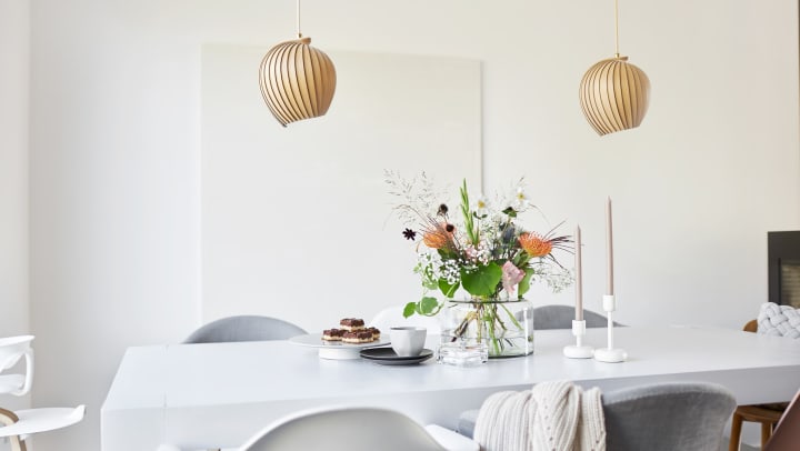 A decorated white dining table in a bright room with colorful flowers and a simple flower vase.