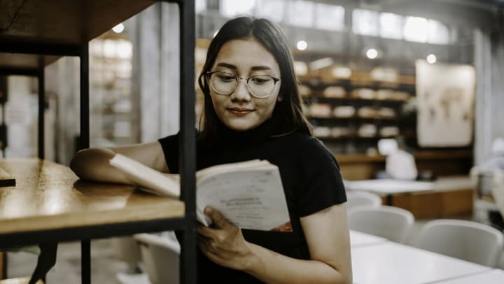 Young female reading a book while leaning against a bookshelf | Ector County Library in Odessa