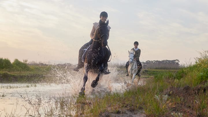 A smiling girl rides a horse through a shallow body of water.