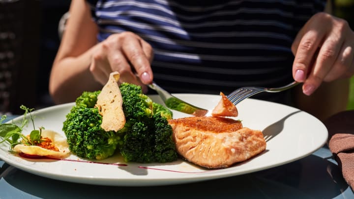 Close-up of a woman eating salmon and broccoli.