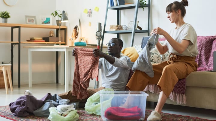 Young couple sitting on the floor and putting clothes in order into boxes at home.
