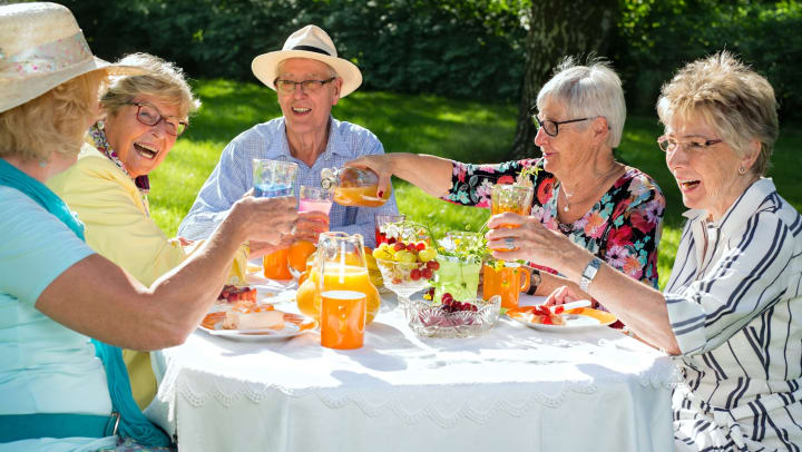Five senior adults enjoying dessert outdoors raising their drinking glasses about to make a toast