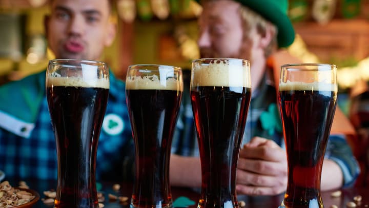 Close-up of full glasses of dark beer with foam placed on table with nut shells