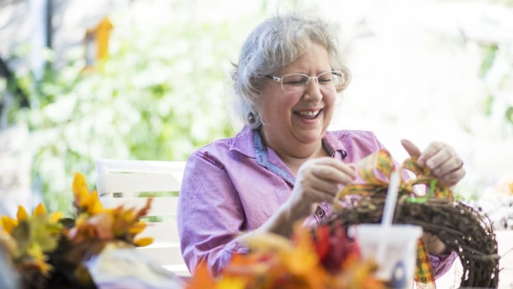 A smiling older woman creating a fall wreath.
