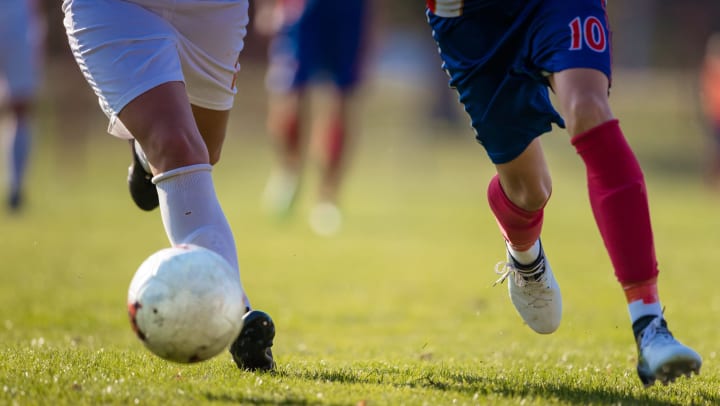 Two soccer players chasing after a soccer ball