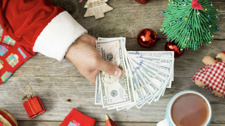 A Santa suit-sleeved arm extends fanned out cash to customer looking to save money around Christmas.