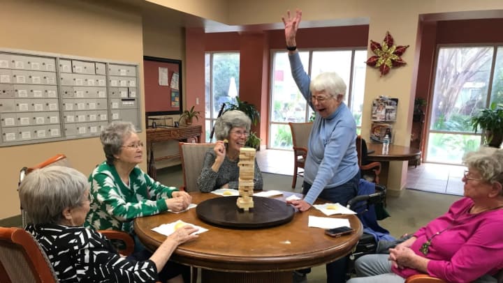 women seated around a table playing Jenga with one woman raising a fist in victory