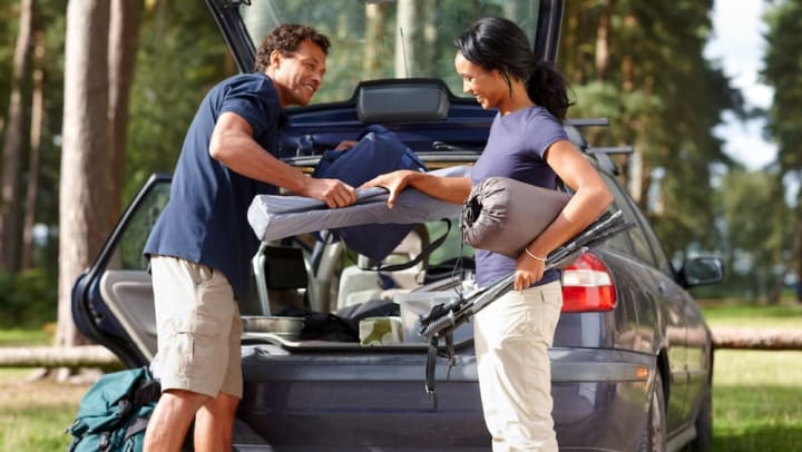 A man and woman loading camping gear into the back of a car.