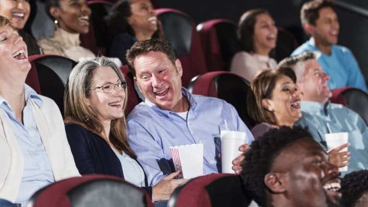 A group of people in a theater setting all laughing as they look toward the source of the entertainment