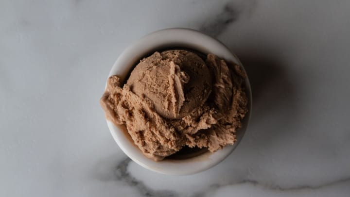 A scoop of chocolate ice cream in a bowl on a marble countertop.