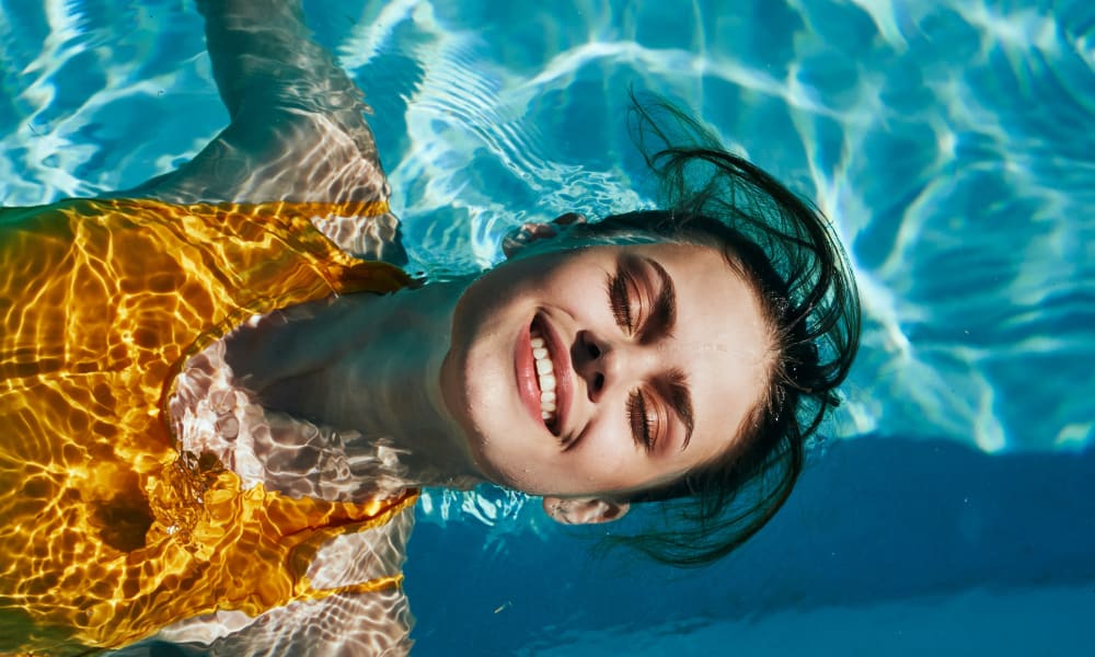 Resident smiling while floating on her back in the swimming pool at Stone Ranch Townhomes in Seguin, Texas