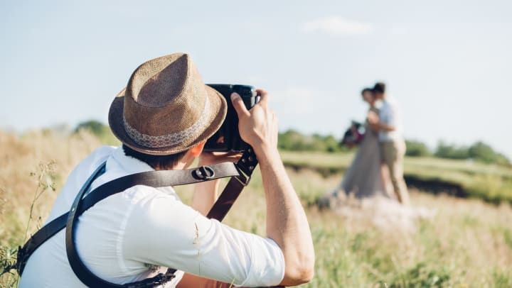 A wedding photographer taking images of a bride and groom in a grassy field | wedding photographers in Charlotte