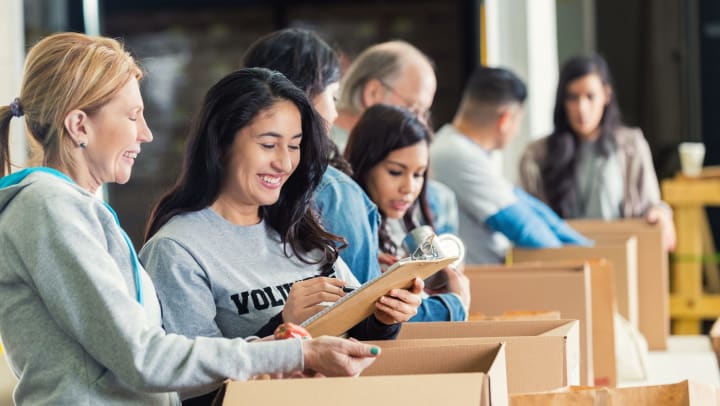 A diverse group of adults packs a row of donation boxes at a food bank.