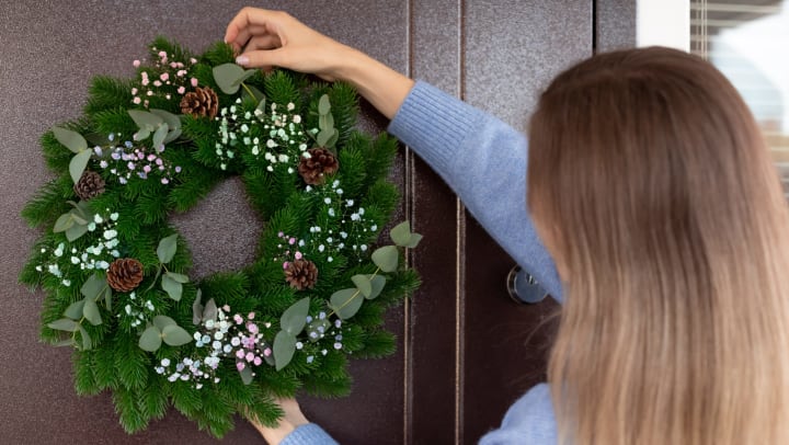 A woman hanging a holiday wreath on her front door.