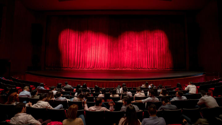 An audience waiting for the red stage curtains to open at a performance