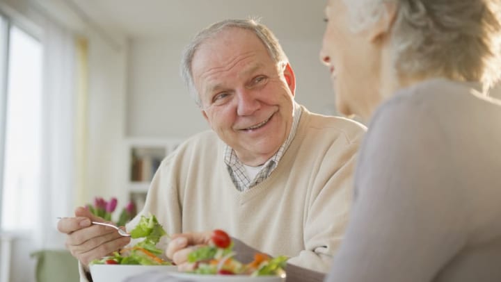 Older man and older woman smiling while eating salad
