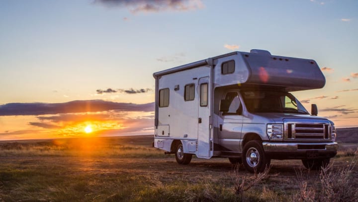 A small RV parked on an unpaved area, with the sun setting in the background