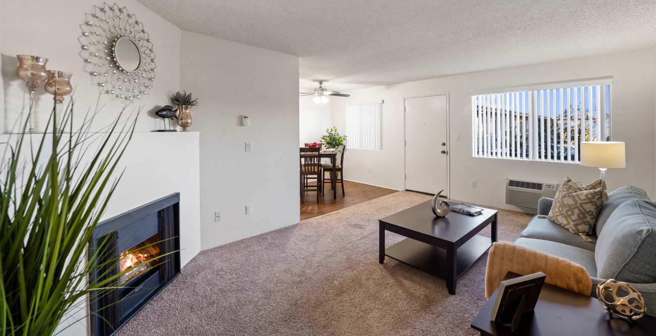 A cozy living room with a lit fireplace, a blue sofa, and a coffee table. In the background is a dining area at The Parkview in Lake Balboa, CA