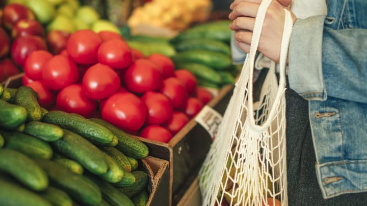 Person with a bag in their hand shopping and looking at fruits and vegetables.