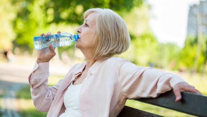 Resident sitting on a park bench drinking bottled water outdoors with trees in background