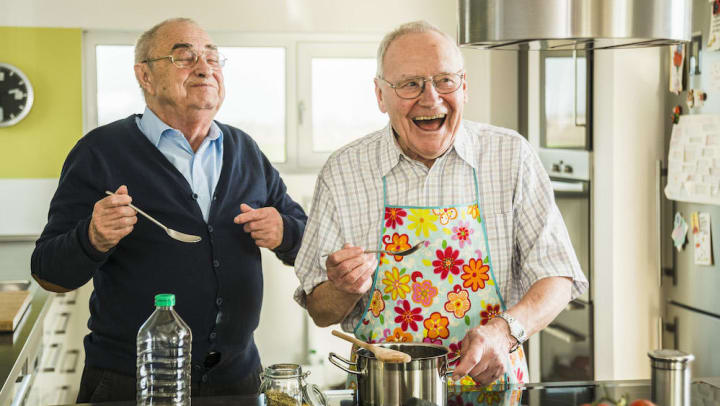 Two happy senior friends cooking in kitchen