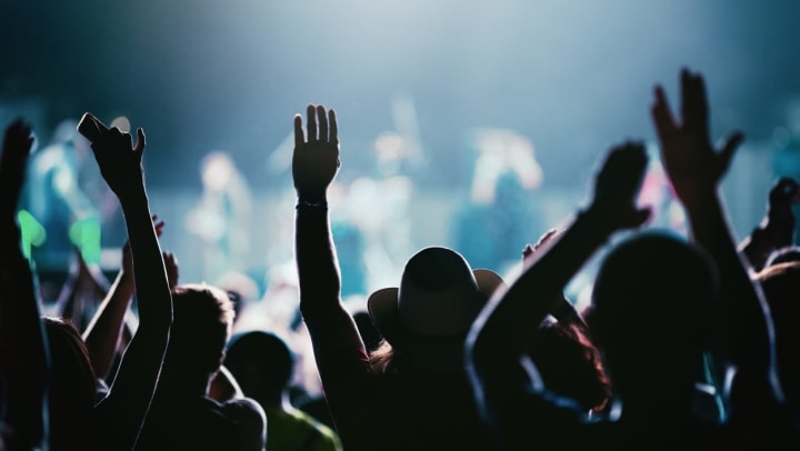 Rear view of a large group of people with their hands in the air at a concert performance | venues in Fort Worth