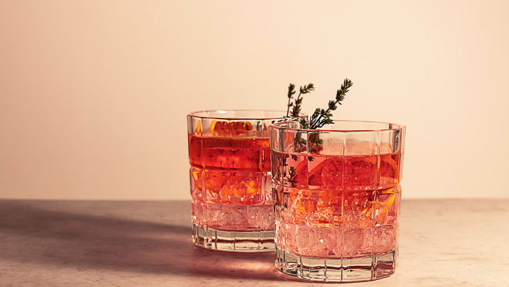 Two cocktail glasses filled with a pink gin cocktail with red blood orange and ice and a garnish.