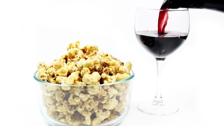 A bowl of popcorn next to a glass of wine.