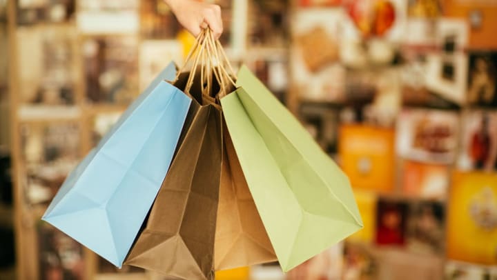 Hand holding four paper shopping bags of various colors | shops in Ooltewah
