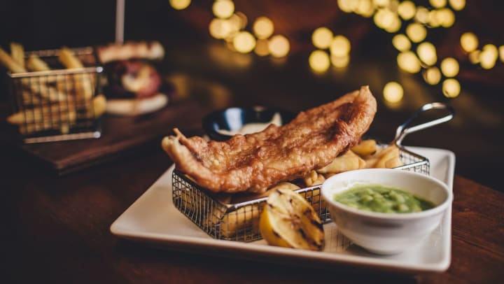 Crispy fish and chips in a metal basket and grilled lemon on a plate with twinkling lights in the background