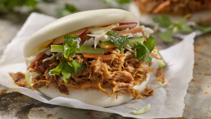 Steamed bao buns with pulled pork with carrots, coleslaw and cilantro with a savory sauce