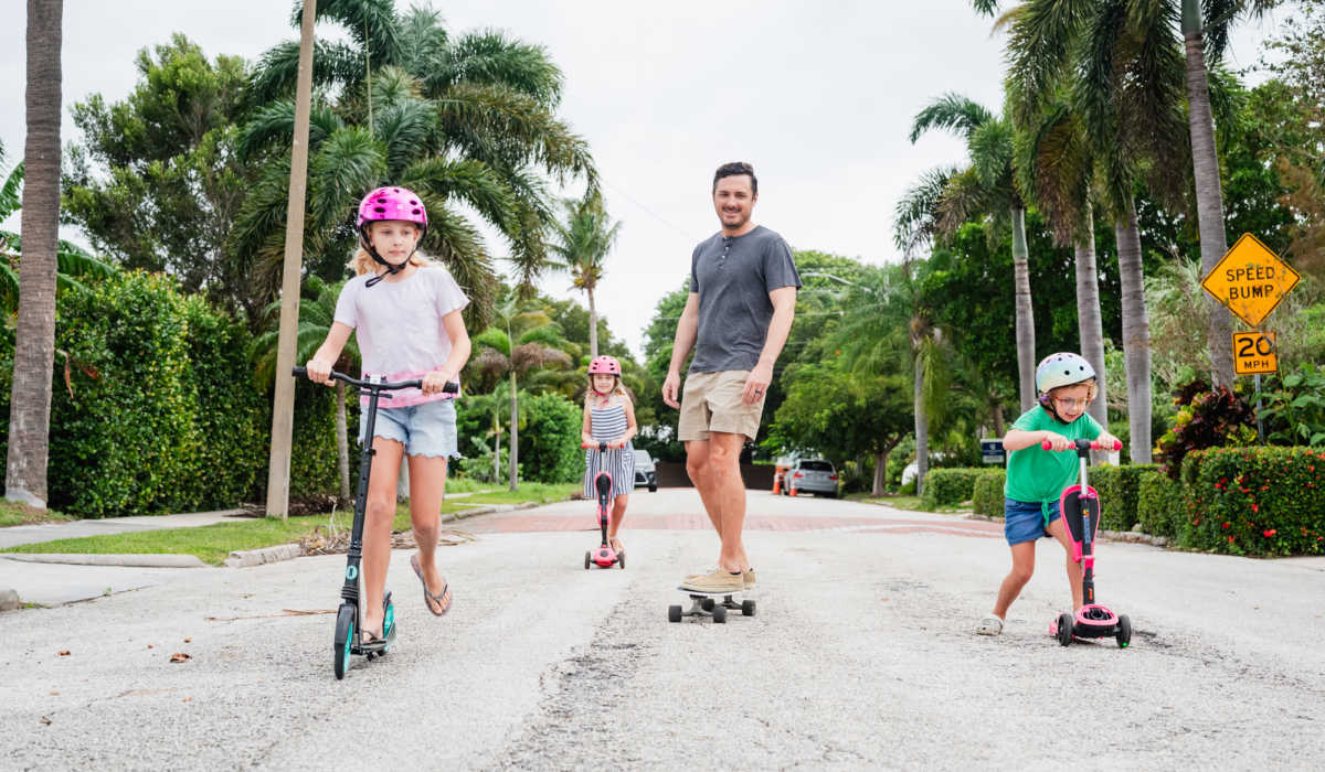 Family enjoying scooters and skateboard on sunny street at Pheasant Run Townhomes in Harrisonburg, Virginia