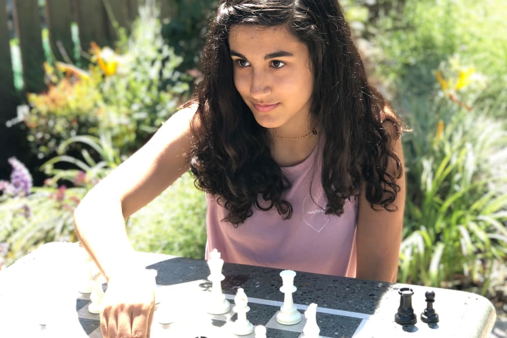 Girl playing chess at an outdoor chess table at Village Green Apartments in Cupertino, California