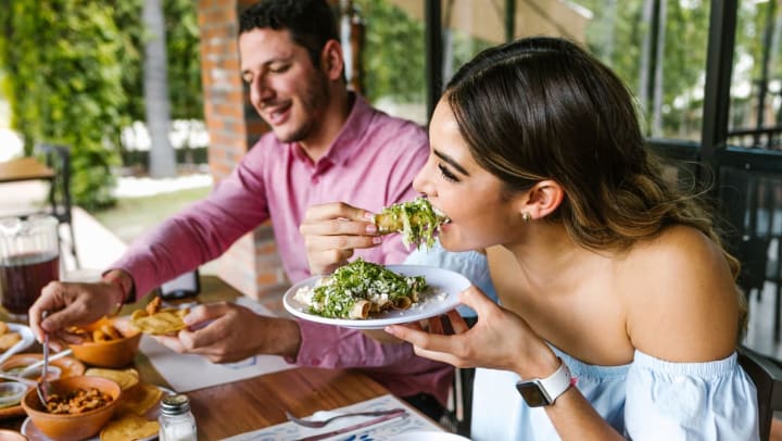 A man and woman biting into food at a restaurant | New Mexican cuisine in Santa Fe