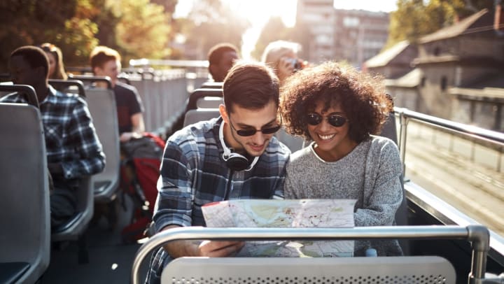 A man and woman looking at a map while riding on the open-air level of a double-decker bus during a city tour in Savannah.