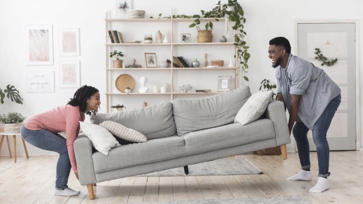 A smiling couple moving a sofa in their living room.