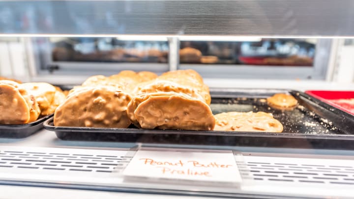 Peanut Butter Praline cookies on a tray in a display case, with a handwritten sign in front.