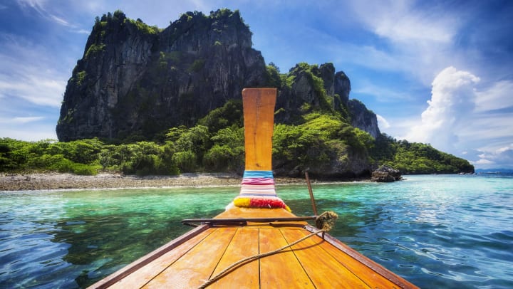 thin boat on blue water facing an island with a large rock formation
