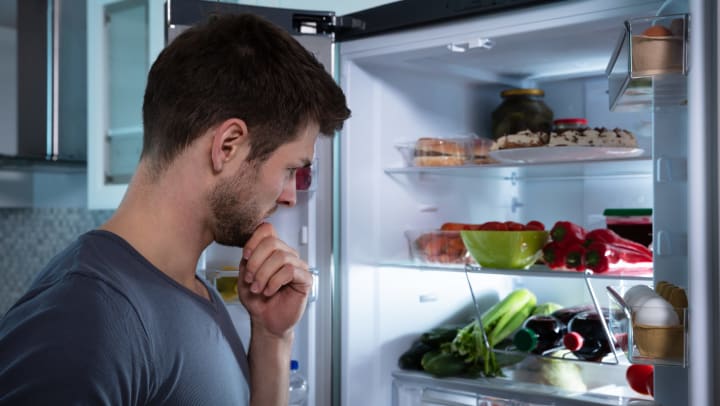 A man contemplating the items sitting inside an open refrigerator.