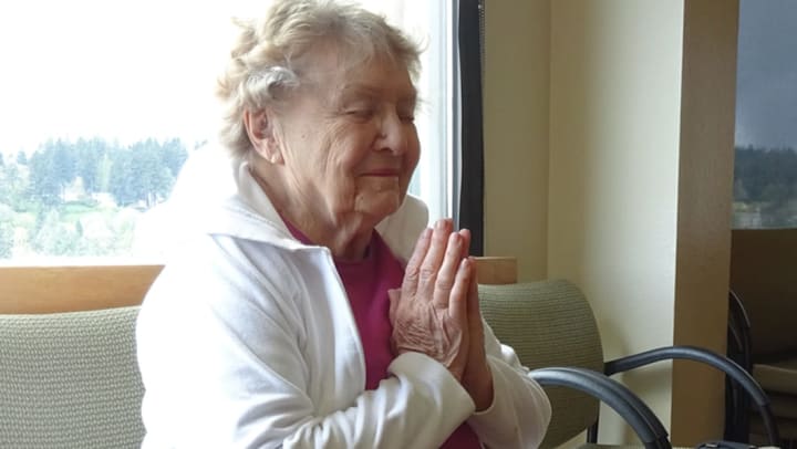 Elderly woman with eyes closed, hands clasped together and lifted up near her chin