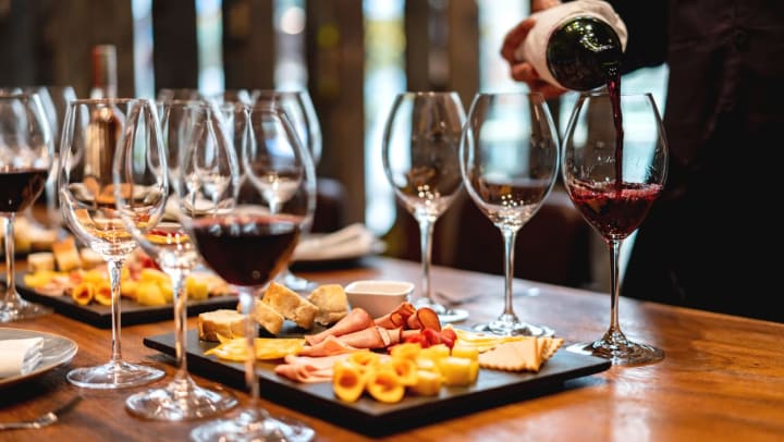 Close up of a charcuterie board and a server pouring wine into glasses at a wine bar
