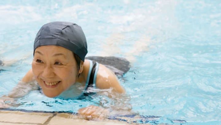 Senior woman smiling while holding on to the ledge of a pool 