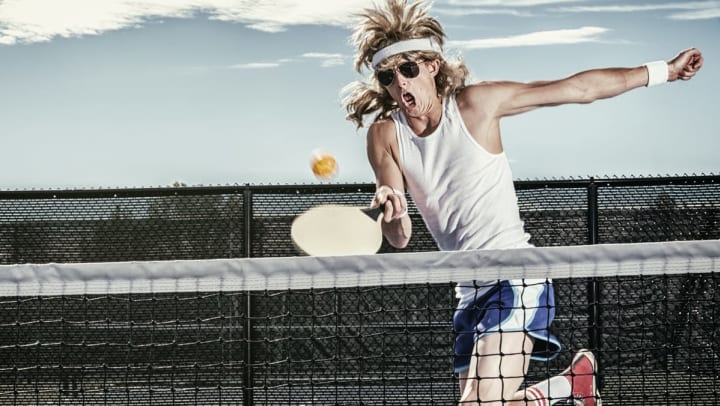 A guy wearing aviators and white sweatbands swings a racket while playing pickleball in Jacksonville.