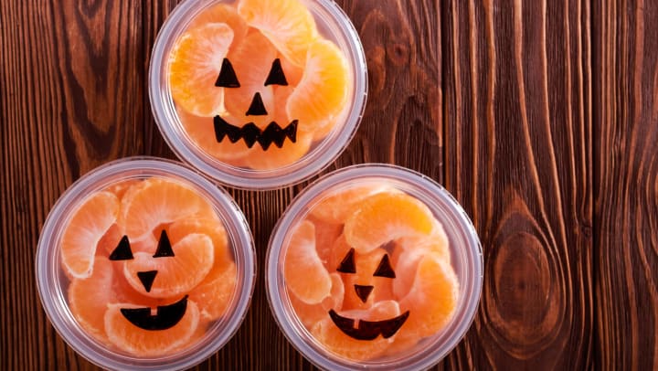 Three cups of tangerine slices with jack-o’-lantern faces drawn on the lids. 