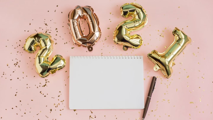 Blank page in a notebook with 2021 gold foil balloons above and a pink backdrop.