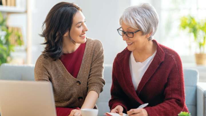 Daughter and senior mother looking at computer with notebook and pen in hand