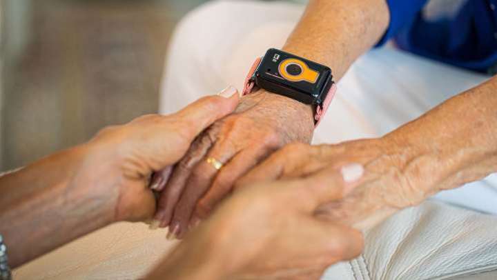 picture of two pairs of hands holding each other with one person wearing a CarePredict Tempo