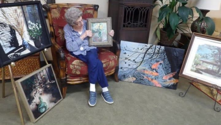 Mary Guthrie is seated among her paintings displayed around her